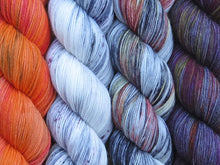 Load image into Gallery viewer, A close up of four skeins of yarn from left to right: variegated orange; variegated white and grey with black and purple speckles; variegated white, grey, black, yellow and rust; and variegated grey with yellow, orange, and purples (Cray Floral Twenty Four Birds MKAL Yarn Kit on Tough Stocking)
