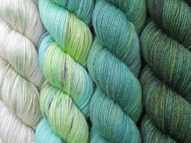 A close up of four skeins of yarn in various shades of greens from variegated cream with green and brown on the left through to tonal deep greens on the right (Endor Geogradient Yarn Kit on Blue Chip Stocking)