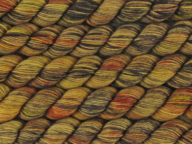 A close up of variegated golden yellow, ebony, honey and rust mini skeins of superwash merino and nylon 4ply fingering sock yarn arranged horizontally (Honeyant on Tough Stocking Mini)