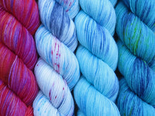 Load image into Gallery viewer, A close up of four skeins of yarn from left to right: variegated pinks, purple and orange; variegated white, blue and grey with blue and pink speckles; variegated aqua, blues and white; and variegated teal and navy with yellow speckles (Huon Wren Twenty Four Birds MKAL Yarn Kit on Tough Stocking)

