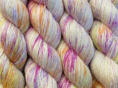 A close up of white with bright speckles of pink, purple, orange and yellow coloured skeins of non-superwash baby alpaca, silk and linen 4ply fingering weight yarn (Titillation on Spinifex)
