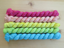 Load image into Gallery viewer, Five light bright rainbow coloured mini skeins of yarn lined up horizontally on a pale wooden background