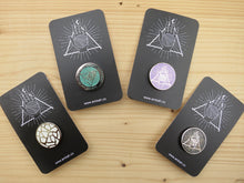 Load image into Gallery viewer, Four enamel pins in various colours, each on a black card with Ambah O'Brien's Knitterati logo, arranged on a pale wooden background