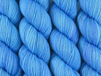 A close up of bright semi-solid medium to light blue with hints of darker blue-violet coloured skeins of superwash merino and nylon 4ply fingering sock yarn (Autumn Sky on Tough Stocking)