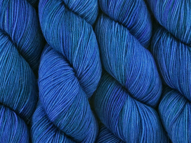 A close up of variegated medium blue with hints of teal green and blue-violet coloured skeins of superwash merino and nylon 4ply fingering sock yarn (Bass Strait on Tough Stocking)