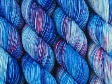 A close up of variegated brilliant aqua blue with splashes of magenta, purple and white coloured skeins of superwash merino and nylon 4ply fingering sock yarn (Bikini Atoll on Tough Stocking)