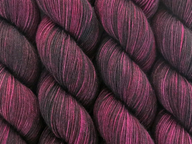 A close up of variegated black, maroon, plum and wine coloured skeins of superwash merino and nylon 4ply fingering sock yarn (Blackened Rose on Tough Stocking)
