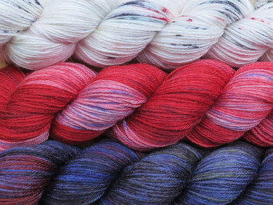 A close up of three variegated skeins of yarn from white with red and black speckles at the top to reds and pink with blue speckles in the middle to blues, red, black and yellow at the bottom (Blood Moon - Ocean Moon MKAL Yarn Kit on Silk Stocking)