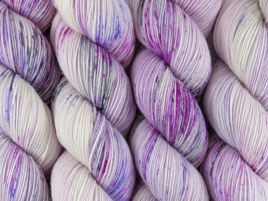 A close up of variegated white with speckles of black, fuchsia and purple coloured skeins of superwash merino and nylon 4ply fingering sock yarn (Candy Is Dandy on Tough Stocking)