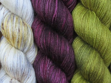 Load image into Gallery viewer, A close up of three variegated skeins of yarn from white with gold and grey with brown speckles on the left; to deep pink maroon with black in the middle; to semi-solid mid yellow-green on the right (Chocolate Mimosa Flower Yarn Kit on Silk Stocking)
