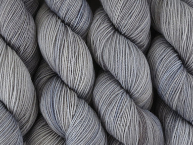 A close up of semi-solid grey with hints of silver, graphite and steel blue coloured skeins of superwash merino and nylon 4ply fingering sock yarn (Fog Bound on Tough Stocking)