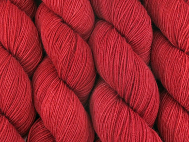 A close up of semi-solid medium red with hints of maroon and crimson coloured skeins of superwash merino and nylon 4ply fingering sock yarn (Japonica on Tough Stocking)