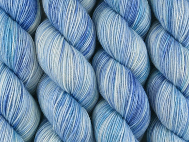 A close up of variegated white, blues and teal coloured skeins of superwash merino and nylon 4ply fingering sock yarn (Katabatic Winds on Tough Stocking)