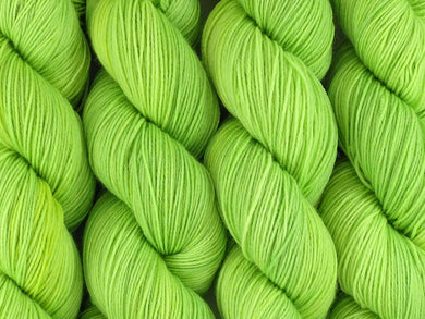 A close up of semi-solid light bright lime green with hints of neon yellow and gold coloured skeins of superwash merino and nylon 4ply fingering sock yarn (Limelight on Tough Stocking)