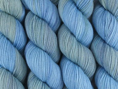 A close up of variegated light blue and sea green with hints of teal, violet blue and grey coloured skeins of superwash merino and nylon 4ply fingering sock yarn (Monkey Mia on Tough Stocking)