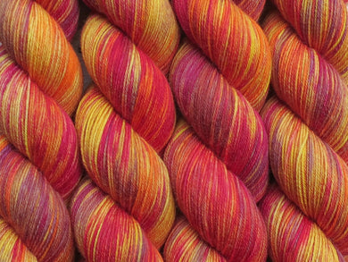 A close up of variegated golden yellow, red, orange and grey coloured skeins of superwash merino and nylon 4ply fingering sock yarn (Nice Melons on Tough Stocking)