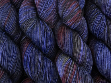 A close up of variegated charcoal, deep blue, violet and red with hints of yellow coloured skeins of superwash merino and nylon 4ply fingering sock yarn (Night's Watch on Tough Stocking)