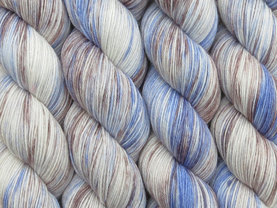 A close up of variegated white with splashes of sky blues and cocoa brown coloured skeins of superwash merino and nylon 4ply fingering sock yarn (Old Flannel Shirt on Tough Stocking)