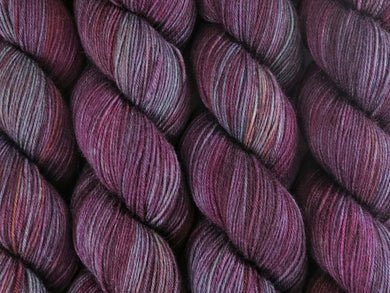 A close up of variegated purple, maroon, orange and mint green coloured skeins of superwash merino and nylon 4ply fingering sock yarn (Purple Smoke Bush on Tough Stocking)