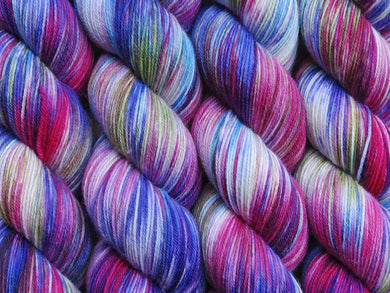 A close up of variegated blues, magenta, white and yellow green coloured skeins of superwash merino and nylon 4ply fingering sock yarn (Rhelma on Tough Stocking)
