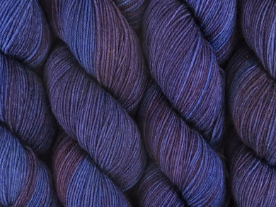 A close up of semi-solid dark blue, midnight blue, deep red-purple and maroon coloured skeins of superwash merino and nylon 4ply fingering sock yarn (Round Midnight on Tough Stocking)