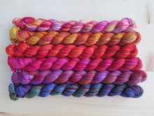Load image into Gallery viewer, Six brightly coloured variegated mini skeins of yarn lined up horizontally on a pale wooden background
