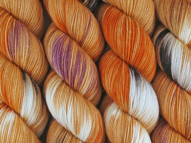 A close up of variegated orange, tan, white, black, maroon and mauve coloured skeins of superwash merino and nylon 4ply fingering sock yarn (Tiger Prawns on Tough Stocking) Edit alt text