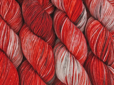 A close up of variegated rich reds with charcoal greys and white coloured skeins of superwash merino and nylon 4ply fingering sock yarn (Twelve Collegia on Tough Stocking)