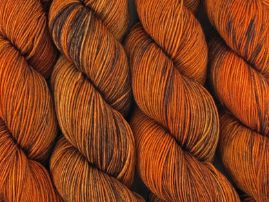 A close up of variegated burnt orange, tangerine and saffron with overtones of caramel and chocolate coloured skeins of superwash merino and nylon 4ply fingering sock yarn (Tyger Tyger on Tough Stocking)