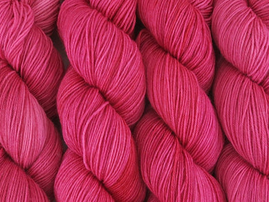 A close up of semi-solid medium pink with hints of crimson and carmine coloured skeins of superwash merino and nylon 4ply fingering sock yarn (Watermelon on Tough Stocking)