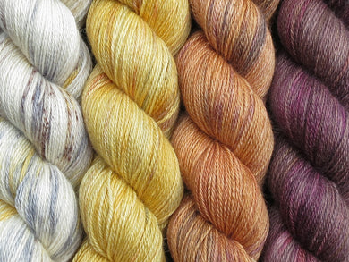 A close up of four skeins of yarn in various shades of yellows and browns from ecru with brown, grey and yellow on the left through to a variegated brown on the right (Arrakis Geogradient Yarn Kit on Blue Chip Stocking)