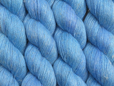 A close up of bright semi-solid medium to light blue with hints of darker blue-violet coloured skeins of non-superwash baby alpaca, silk and linen 4ply fingering weight yarn (Autumn Sky on Spinifex)
