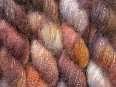 A close up of variegated ebony, chocolate, chestnut and beige brown coloured skeins of superfine kid mohair and silk 2ply lace yarn (Bungil on Kid Glove Lace)