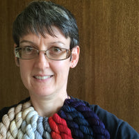 A woman with glasses wearing various coloured mini skeins of yarn around her neck