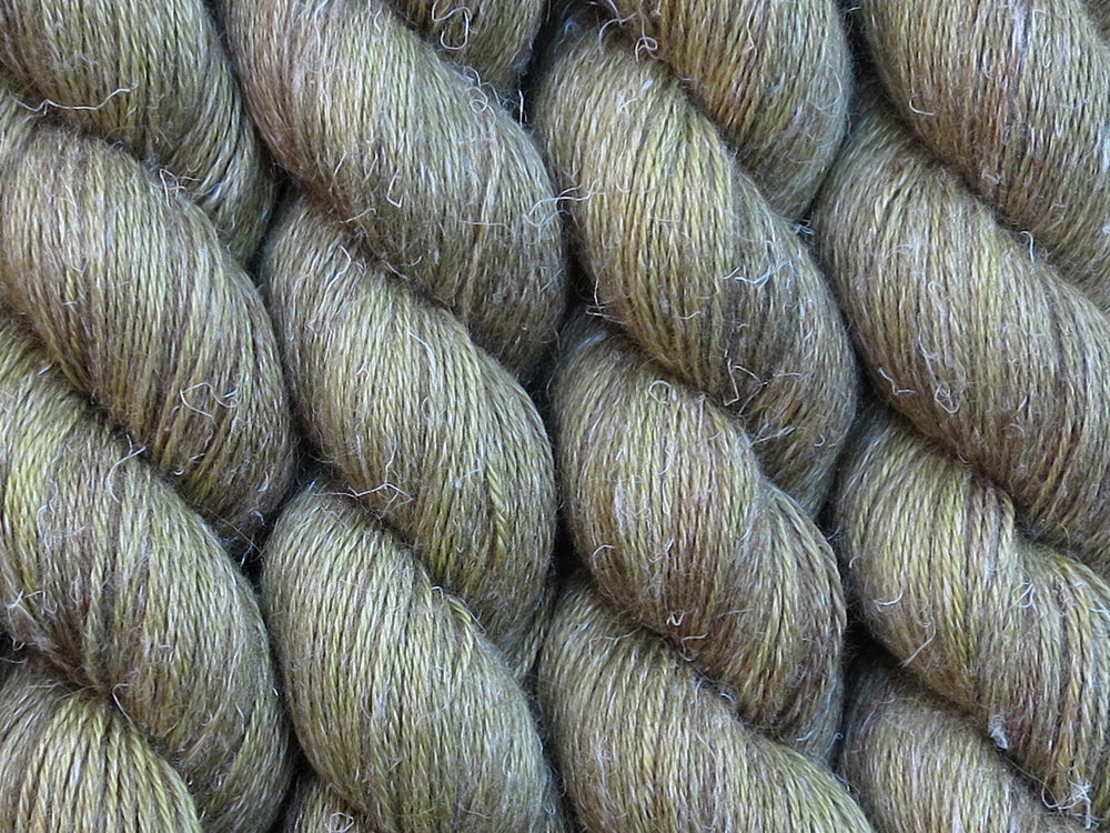 A close up of semi-solid mid-khaki green with hints of brown, chartreuse and golden tan coloured skeins of non-superwash baby alpaca, silk and linen 4ply fingering weight yarn (Fatigued on Spinifex)
