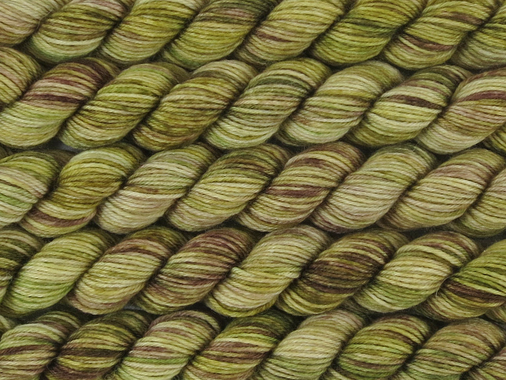 A close up of variegated khaki and forest greens, ecru and brown mini skeins of superwash merino and nylon 4ply fingering sock yarn arranged horizontally (Gone Bush on Tough Stocking Mini)