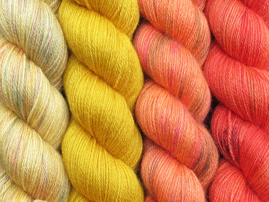 A close up of four skeins of yarn in various shades of yellow and orange from variegated straw yellow on the left through to a variegated orange with black speckles on the right (Kyrian Geogradient Yarn Kit on Blue Chip Stocking)