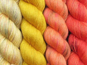 A close up of four skeins of yarn in various shades of yellow and orange from variegated straw yellow on the left through to a variegated orange with black speckles on the right (Kyrian Geogradient Yarn Kit on Blue Chip Stocking)