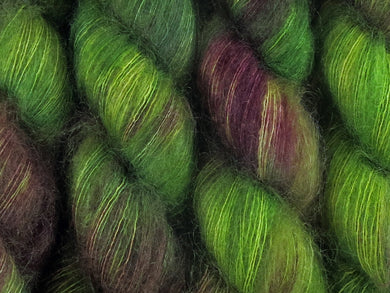 A close up of variegated bright kelly green and maroon with hints of forest and hunter greens, chartreuse and umber coloured skeins of superfine kid mohair and silk 2ply lace yarn (Mesclun Mix on Kid Glove Lace)