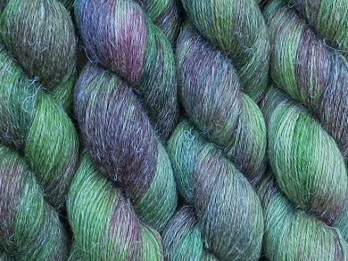 A close up of variegated bright kelly green and maroon with hints of forest and hunter greens, chartreuse and umber coloured skeins of non-superwash baby alpaca, silk and linen 4ply fingering weight yarn (Mesclun Mix on Spinifex)
