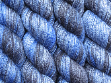 A close up of variegated yarn of black and charcoal with overtones of denim, chambray and navy coloured skeins of superwash bluefaced leicester, silk and cashmere 4ply fingering sock yarn (Moody Blues on Blue Chip Stocking)