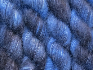 A close up of variegated yarn of black and charcoal with overtones of denim, chambray and navy coloured skeins of superfine kid mohair and silk 2ply lace yarn (Moody Blues on Kid Glove Lace)v