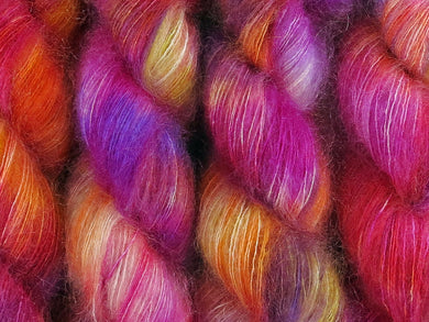 A close up of variegated white, yellow, orange, pink and purple coloured skeins of superfine kid mohair and silk 2ply lace yarn (Much Ado About Knockers on Kid Glove Lace)