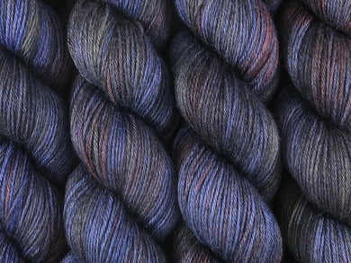 A close up of variegated charcoal, deep blue, violet and red with hints of yellow coloured skeins of superwash merino and silk 4ply fingering sock yarn (Night's Watch on Silk Stocking)