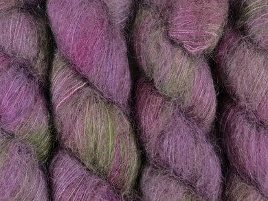A close up of variegated purple, violet and green with hints of hot pink and beige coloured skeins of superfine kid mohair and silk 2ply lace yarn (Purple Sea Urchin on Kid Glove Lace)
