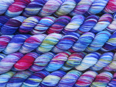 A close up of variegated blues, magenta, white and yellow green mini skeins of superwash merino and nylon 4ply fingering sock yarn arranged horizontally (Rhelma on Tough Stocking Mini)