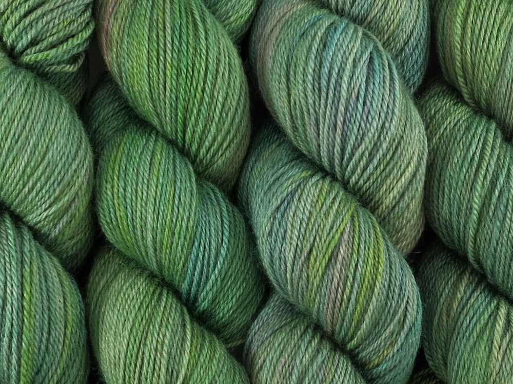 A close up of variegated light grey-green with hints of pink, sulphur yellow and deep jade green coloured skeins of superwash bluefaced leicester, silk and cashmere 4ply fingering sock yarn (Samphire on Blue Chip Stocking)