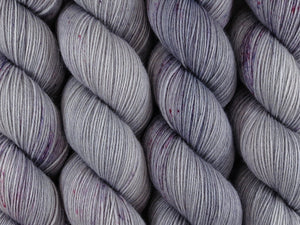 A close up of tonal silver grey with speckles of pink and purple coloured skeins of superwash merino and nylon 4ply fingering sock yarn (Silver Screen on Tough Stocking)