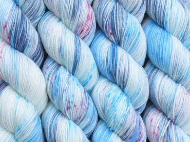 A close up of variegated white, blue and grey with bright pink and blue speckles coloured skeins of superwash merino and nylon 4ply fingering sock yarn (Stardust on Tough Stocking)