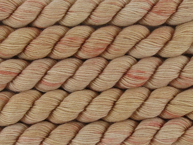 A close up of variegated warm beige tan with coral pink mini skeins of superwash merino and nylon 4ply fingering sock yarn arranged horizontally (Sunburnt on Tough Stocking Mini)